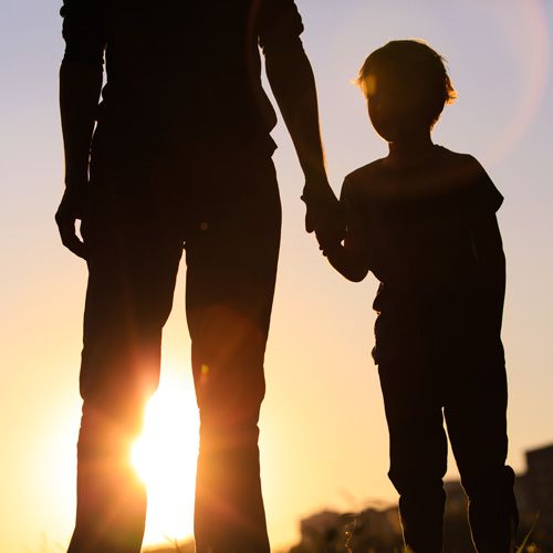 Father holding child's hand at sunset